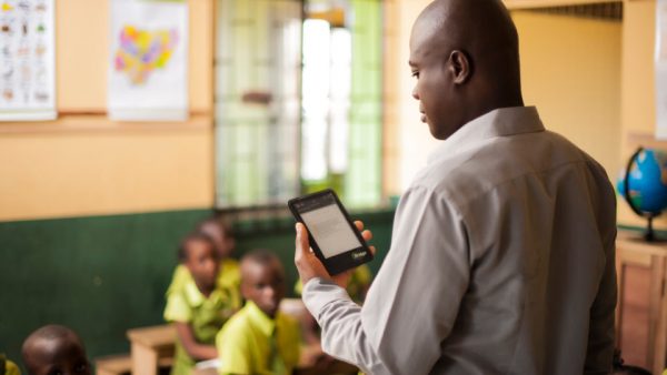 A Bridge teacher holds his teaching computer, and reads a lesson guide.
